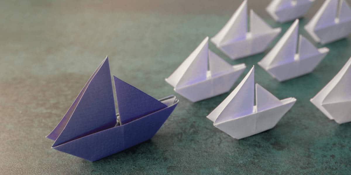 Blue paper boat leading white paper boats